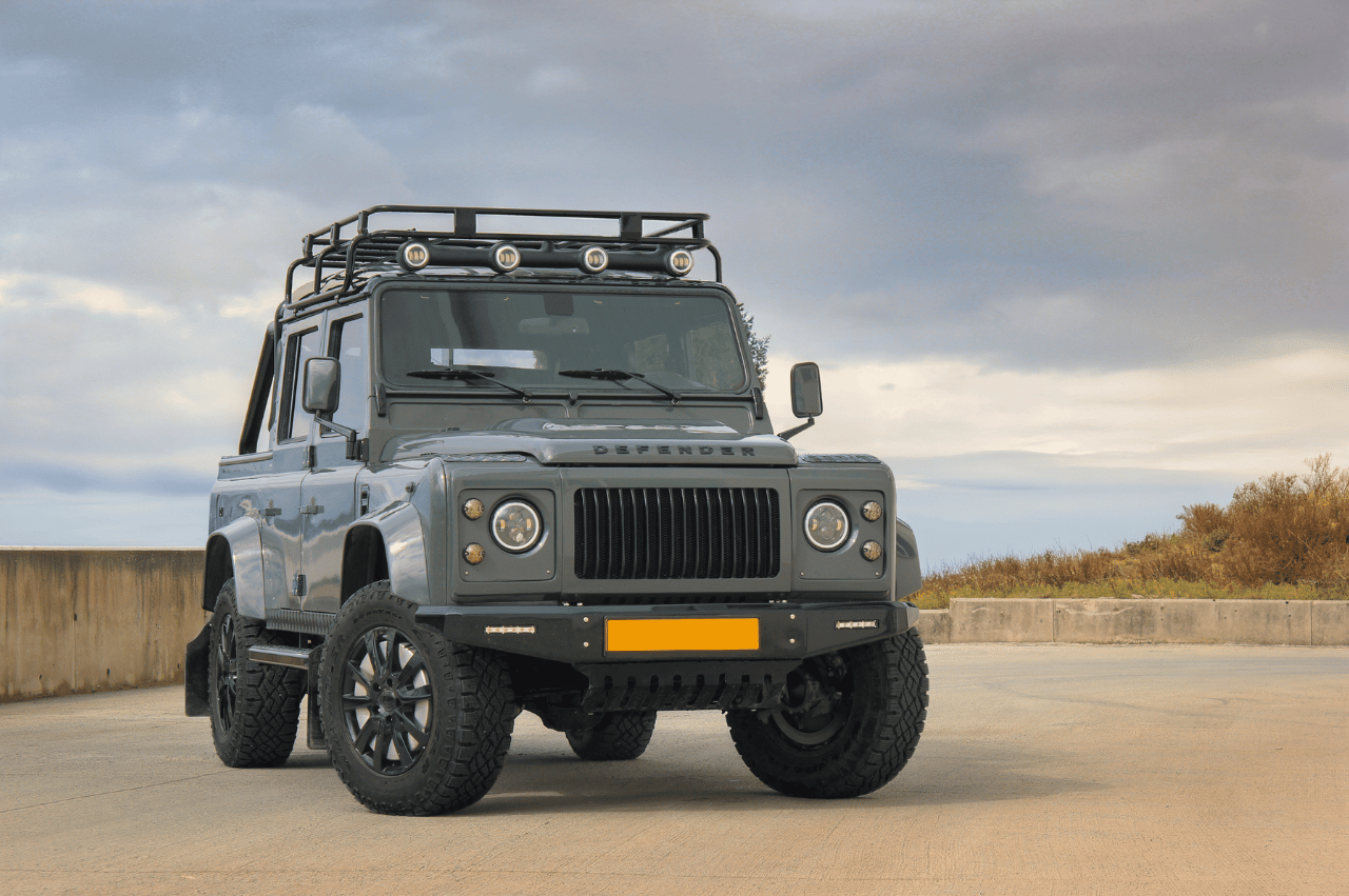A front view of a khaki green defender with a roof rack on a dusk skyline backdrop